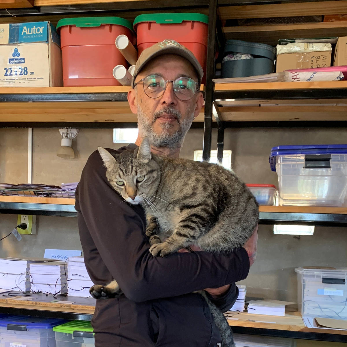 Bookbinder in the bindery holding a cat, surrounded by handcrafted books and supplies.