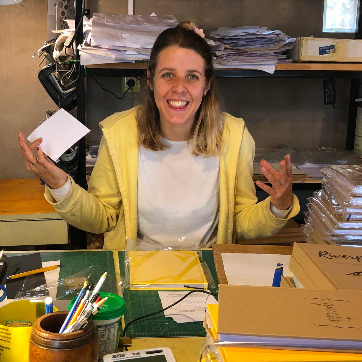 Happy bookbinder in bindery surrounded by stacks of handbound books.