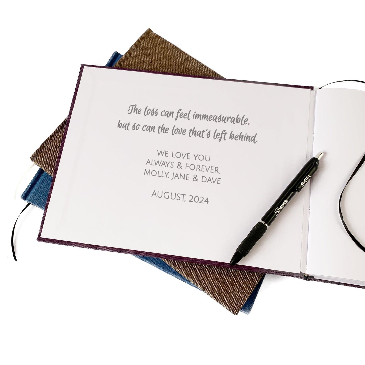 Inside front cover of custom funeral guest book with a meaningful message printed for guests to read. Laying on a stack of heirloom quality memorial service books, with a pen.