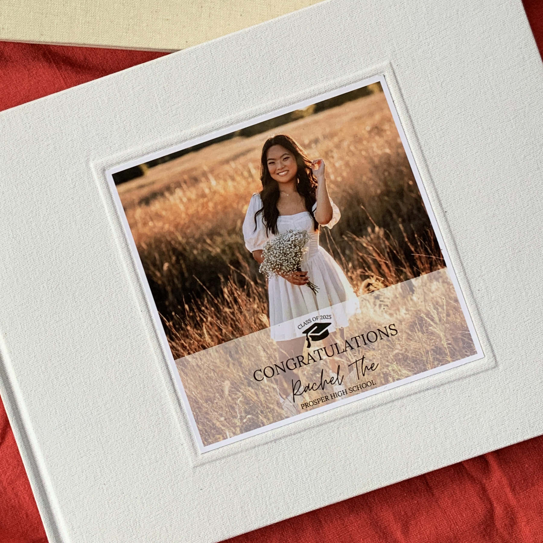 Graduation party guest book with graduation photo on the cover. White linen high quality memory book, personalized text, on a red fabric background. Hard back.