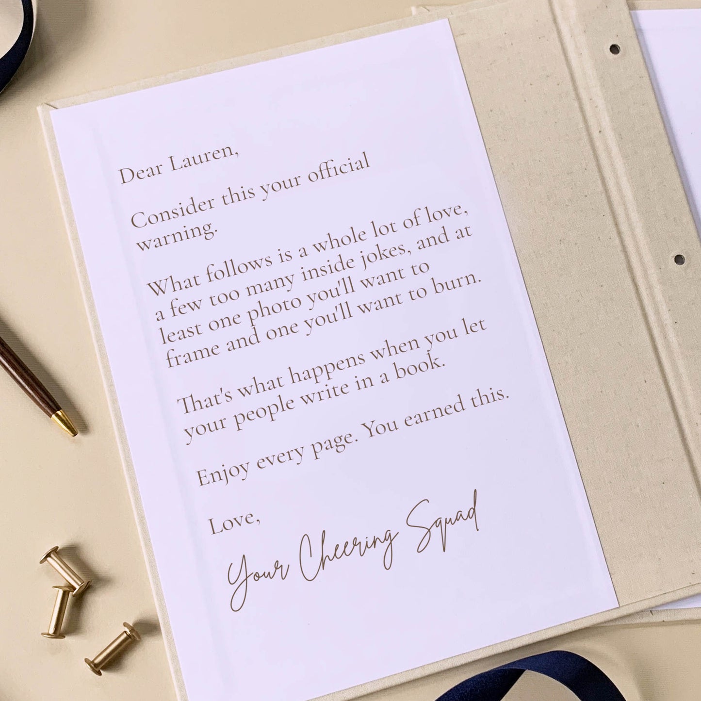 Custom dedication on the inside front cover of a letters to the bride scrapbook, open on a table next to brass screwposts and a pen.