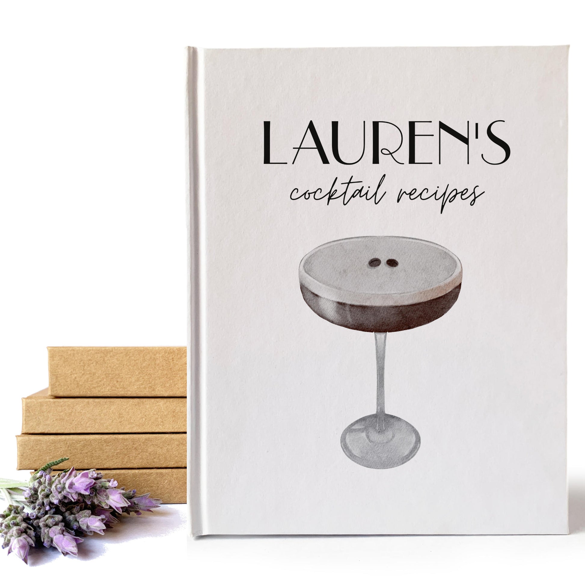 Personalized cocktail book with espresso martini art on the cover and personalized text next to a stack of handbound books and lavender flowers.