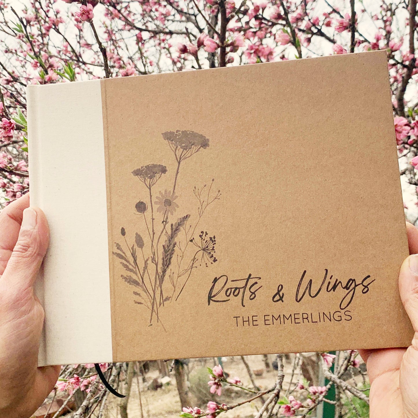 Person holding personalized retirement guest book with cream inen spine canvas. Hardback with personalized wildflower artwork cover design with custom names and text.