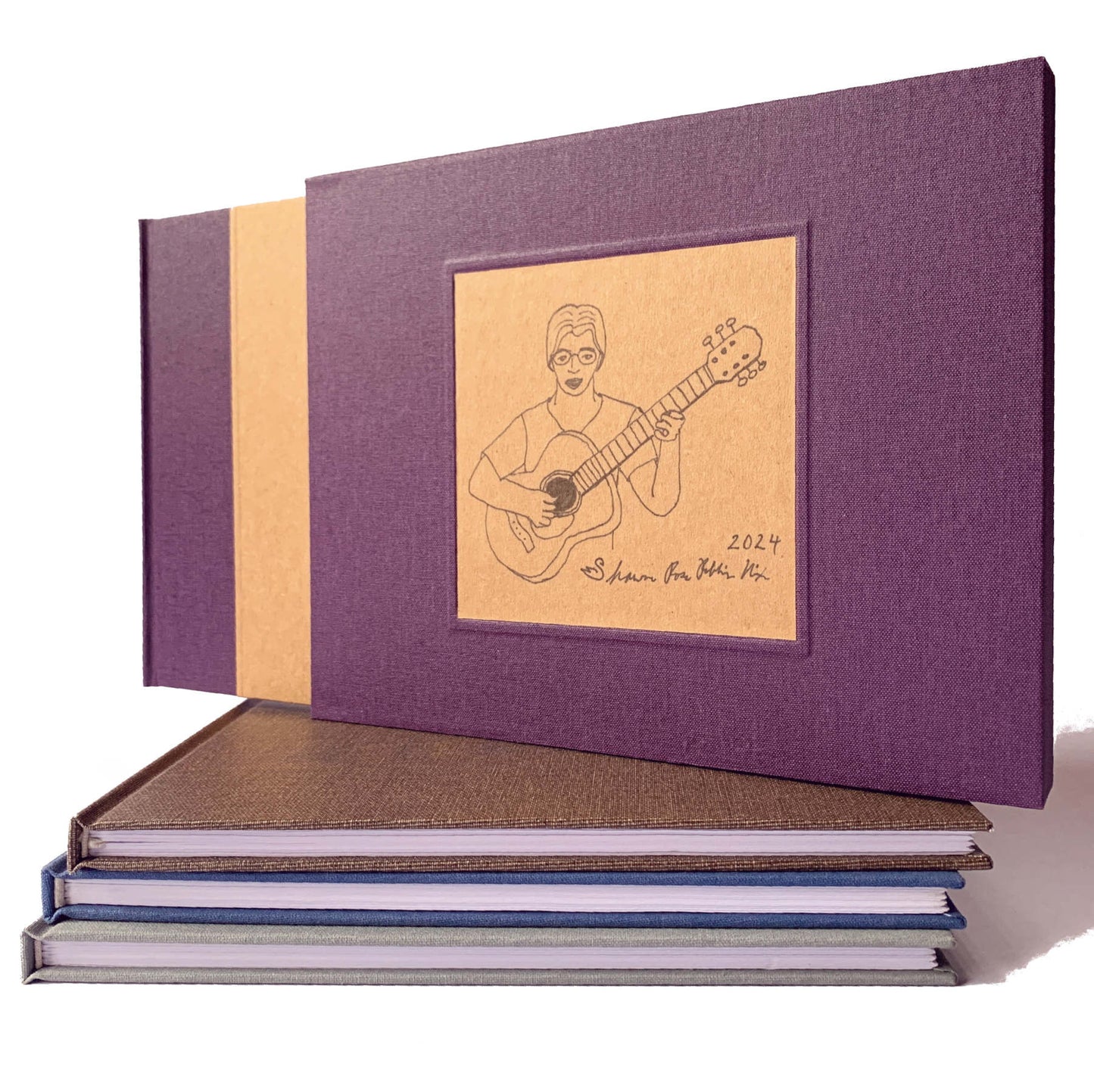 Dark purple book slip case custom made to hold a personalized guest book. Standing on a stack of handbound books, all hardback. Heirloom quality.
