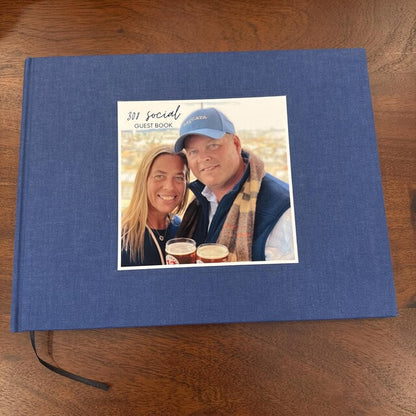 Custom blue linen family home guest book with a photo of two people on a wooden surface