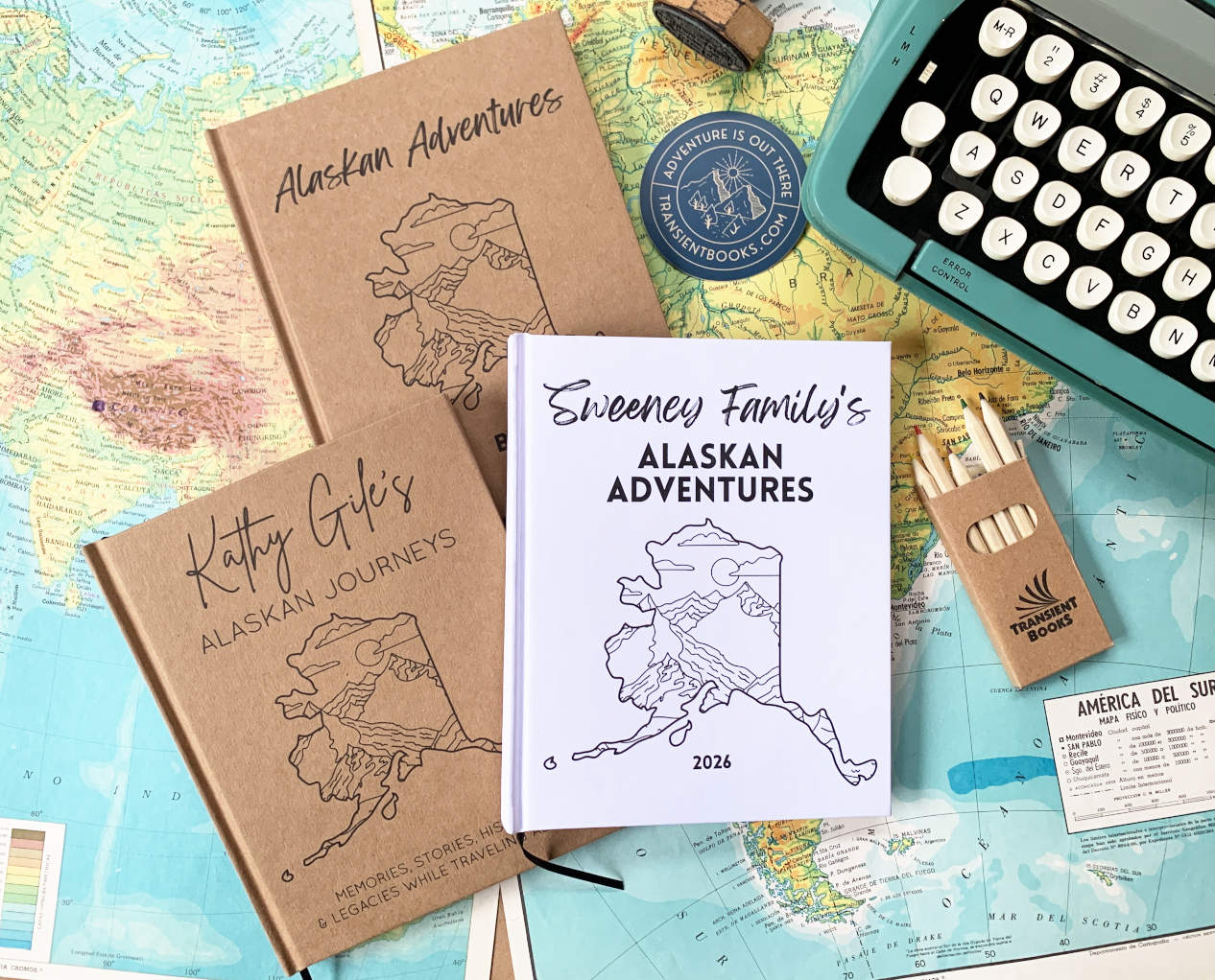 Three personalized Alaska travel journals on a map with stationery items.