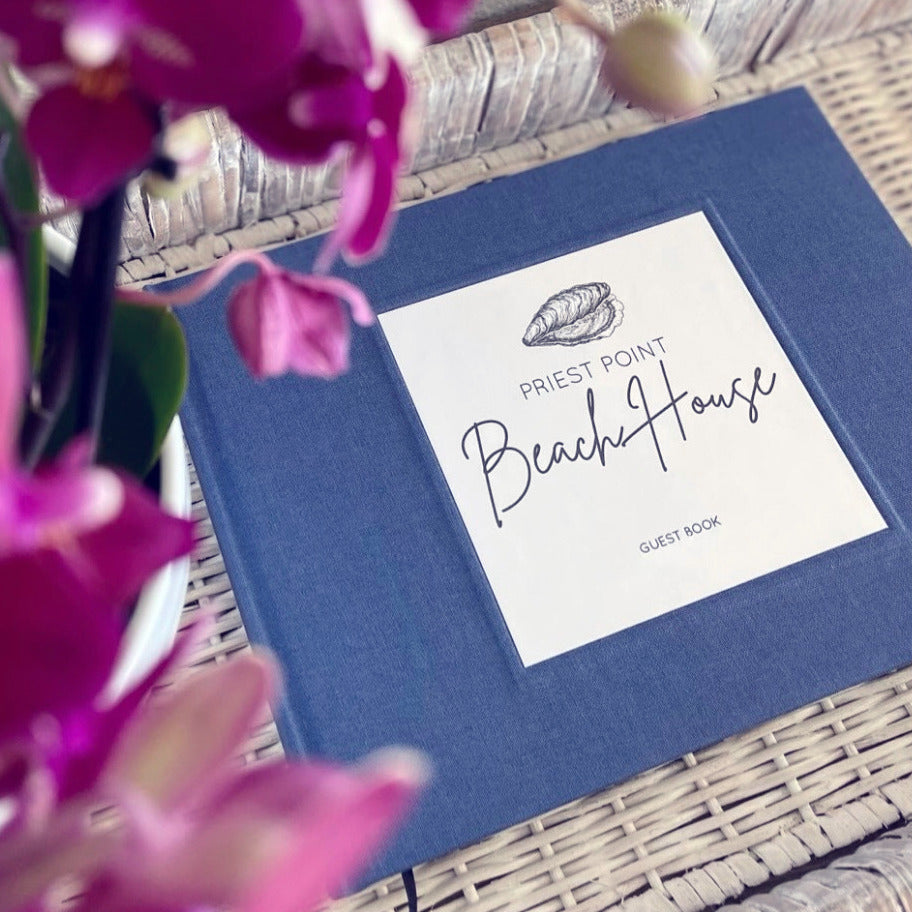 Personalized beach house guest book with blue linen cover. Hardback, handbound, made to order, heirloom quality. Book is on a wicker bench, with orchids.