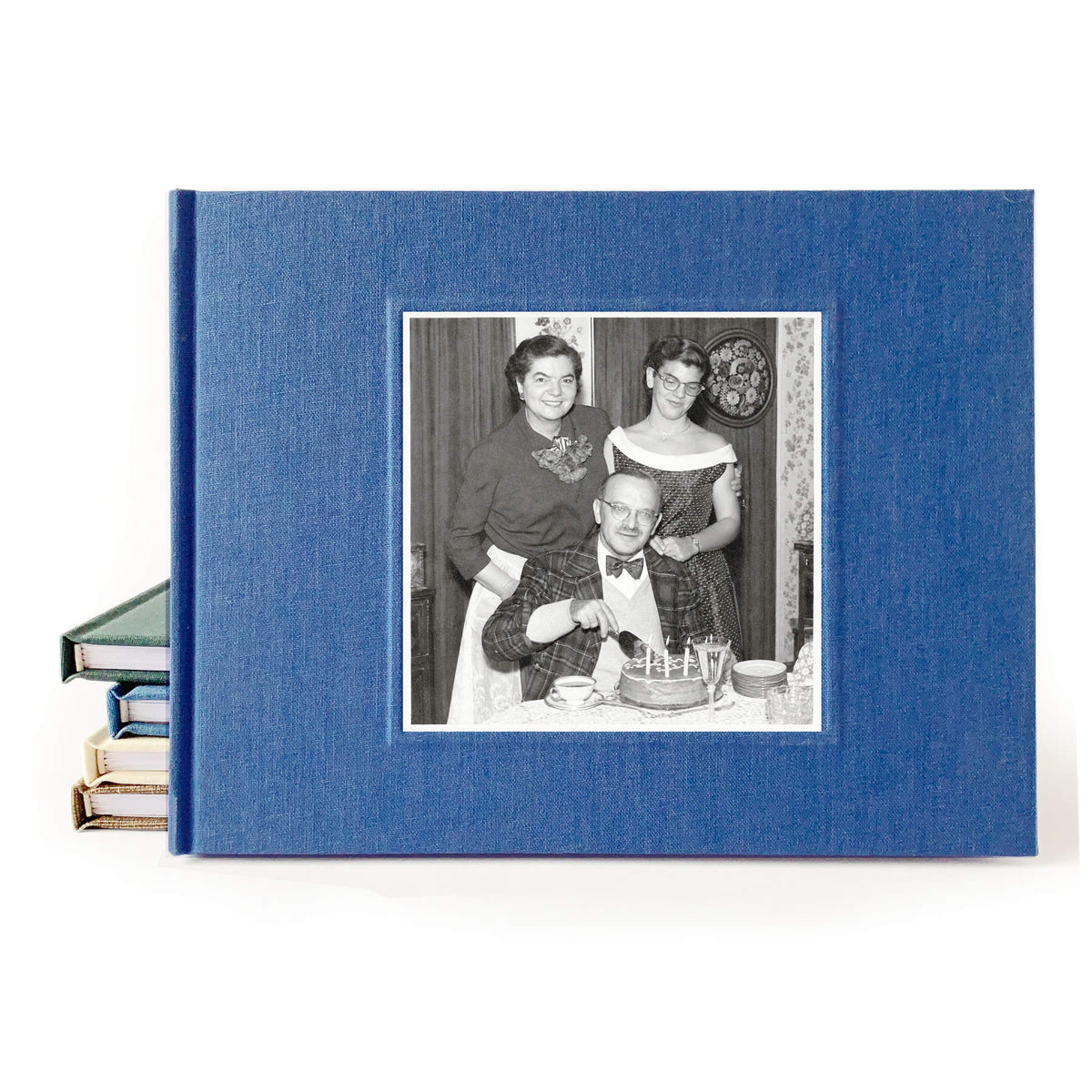 Navy blue linen birthday party guest book with a 1950s family photo in black and white inlaid on the cover. The photo is of a father sitting, about to cut his birthday cake. His daughter and wife stand behind him. All are dressed festively.