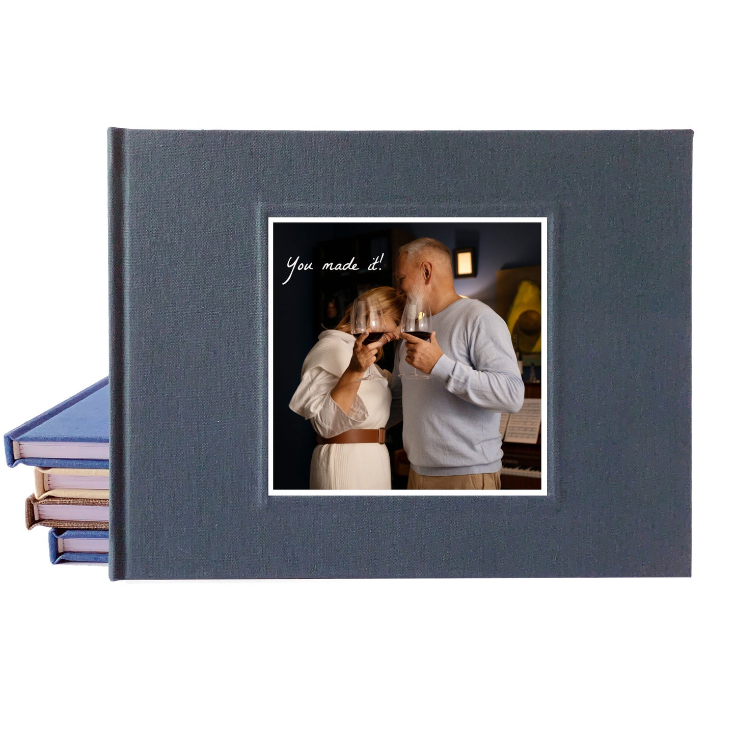 A dark slate gray hardcover guest book shown closed, with a printed sample photo insert on the front and a stack of similar albums fanned out on the left against a white background.