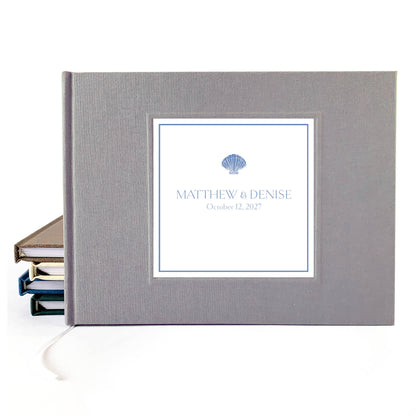 Gray linen hardback wedding guest book with custom names and wedding date on the cover. Seashell artwork incorporated.