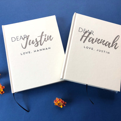 A matching set of couples journals that are letters to husband from wife, letters to wife from husband with custom names on hardback covers. Modern, understated design, hand crafted books on a navy blue surface with orange flowers.
