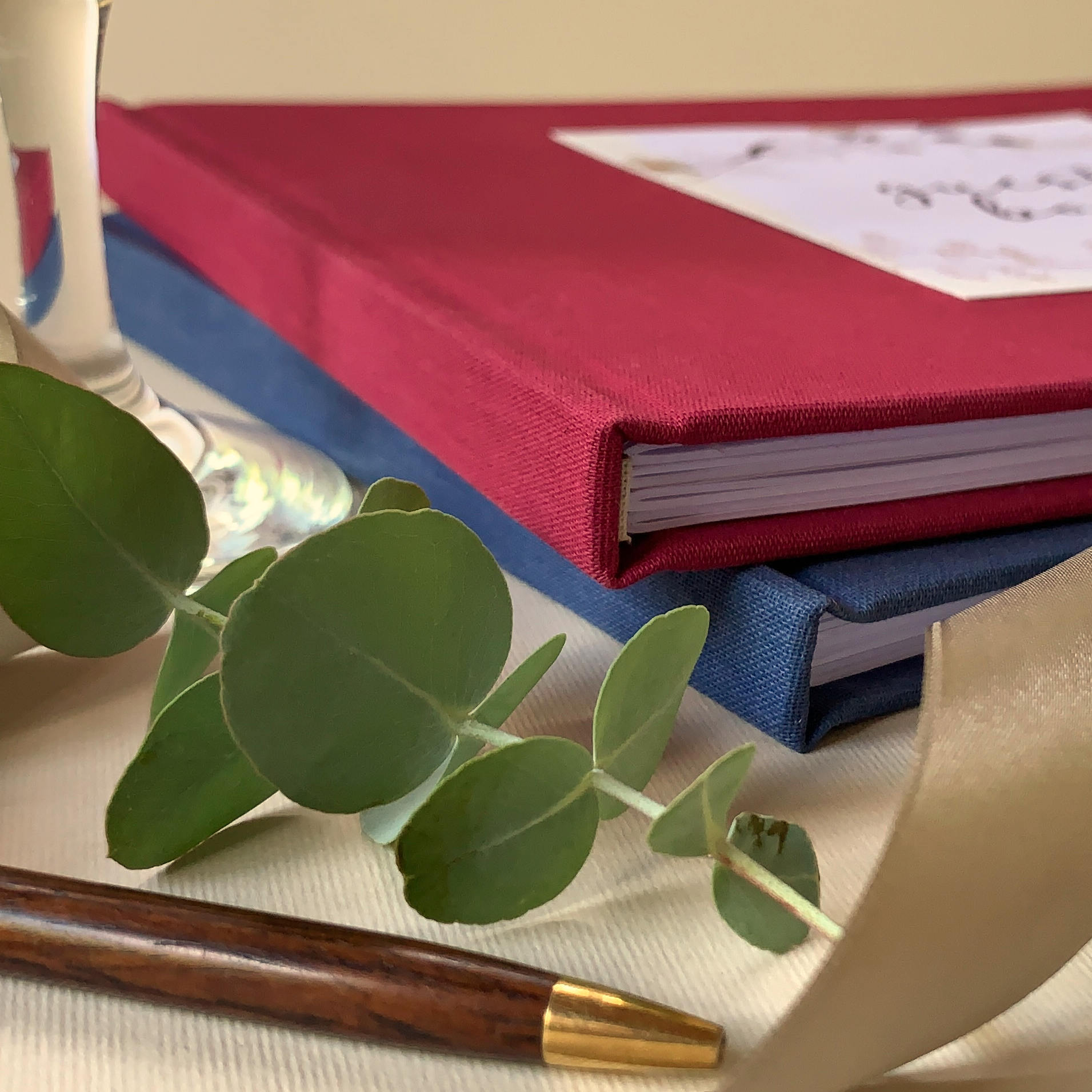 Hand-bound wedding guest books in navy blue and burgundy on a wedding table with pen. Handsewn folios.