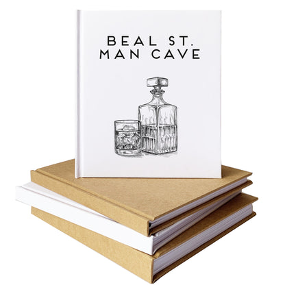 A custom cocktail book with personalized text and whiskey decanter illustration on cover, set on top of a stack of handbound notebooks.