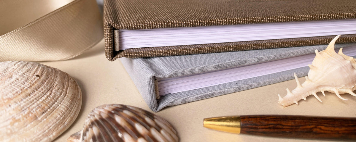 Brown and gray linen guest books with beige ribbon, sea shells and  a pen.