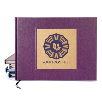 Dark purple linen guest book with a kraft cover inlay with a logo and the text "your logo here" on a white backdrop leaning on another set of handbound books.