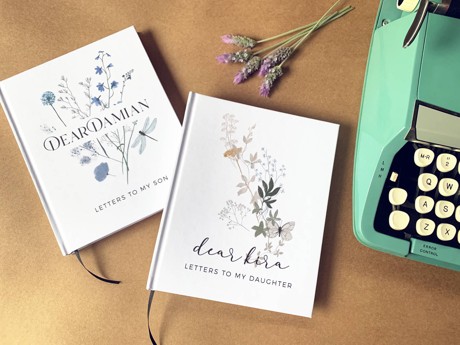 2 custom pregnancy journals with wildflower cover designs and custom  text, on  a table next to fresh lavender and a turquoise typewriter.