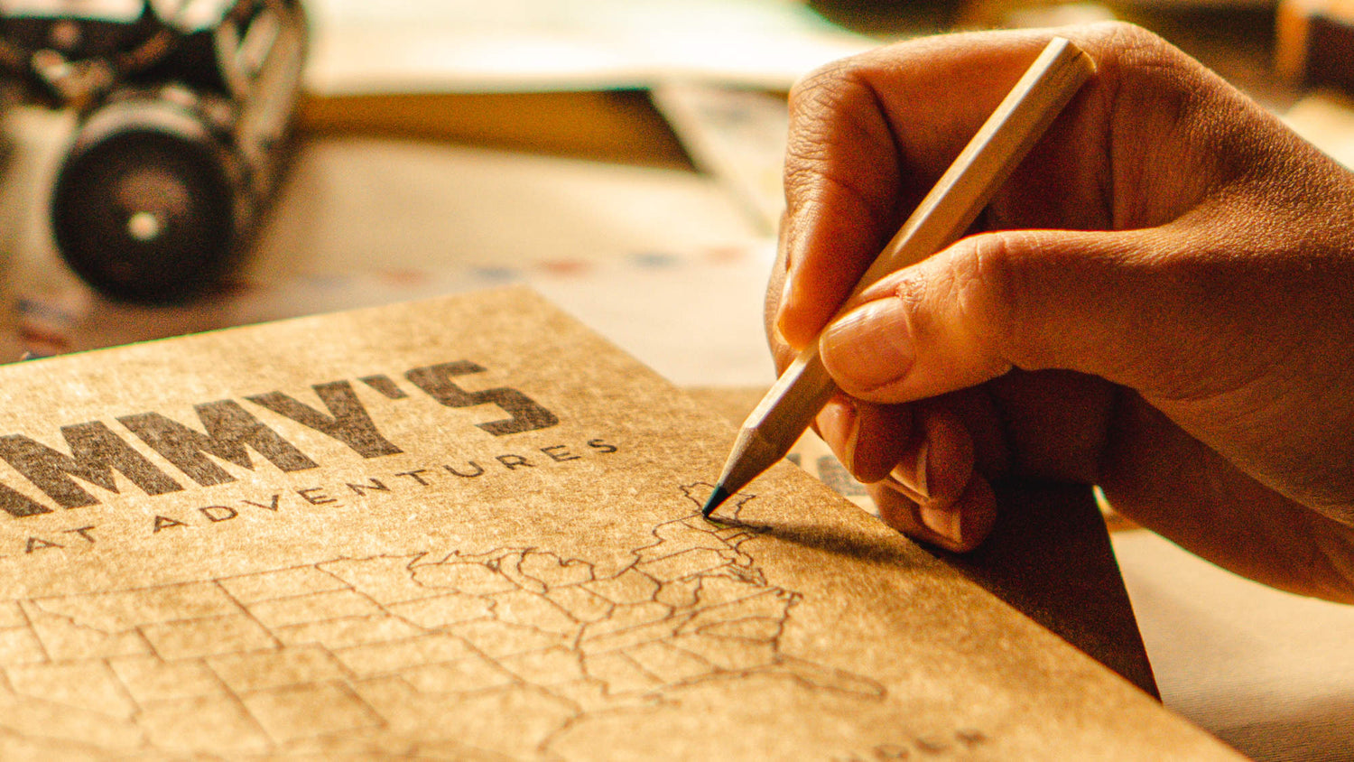 Hand holding a pencil over a custom travel journal with a map for coloring in on a library table.
