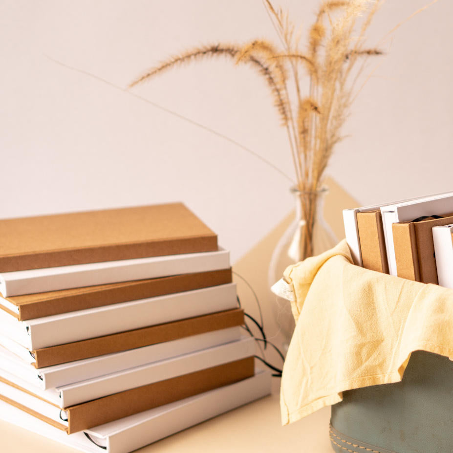 Stack of hand bound books and journals with a vase and plant in the background