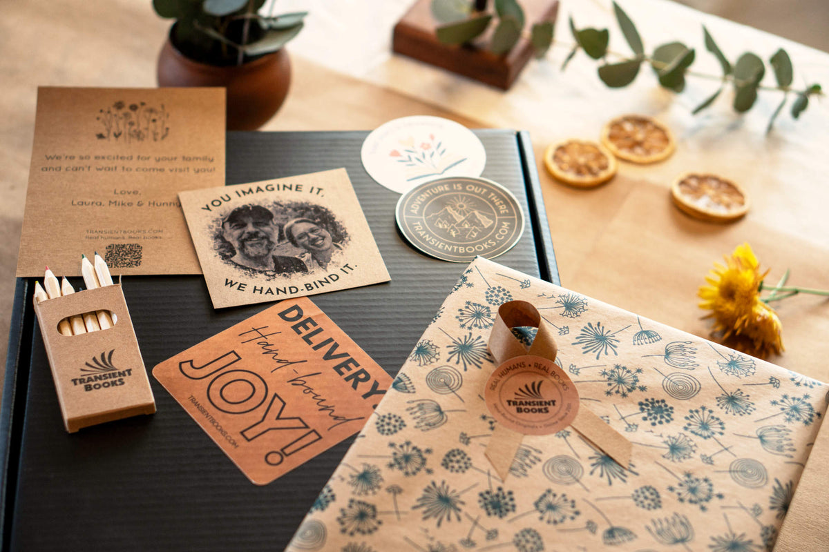 Collection of eco-friendly gifting stickers and gift notes for a book gift box next to a plant and flowers on a wooden surface.