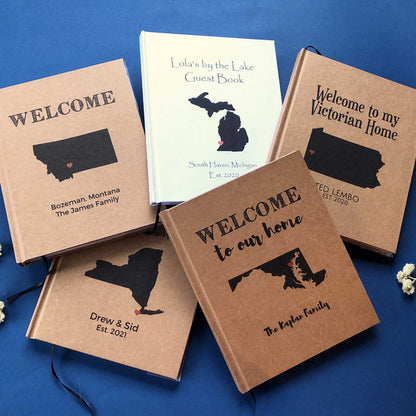 Collection of personalized home guest books in kraft and white hardback covers with custom maps and text on the covers.