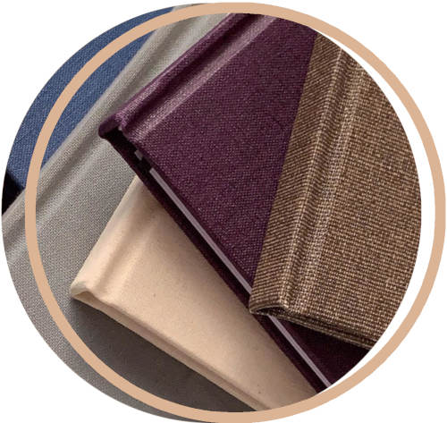 Close-up of various fabric covered hand bound book spines including purple, beige, and brown.