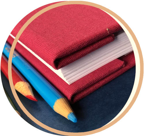 Burgundy screwpost binder spine close up showing inverted spine. Colored pencils on table, too.