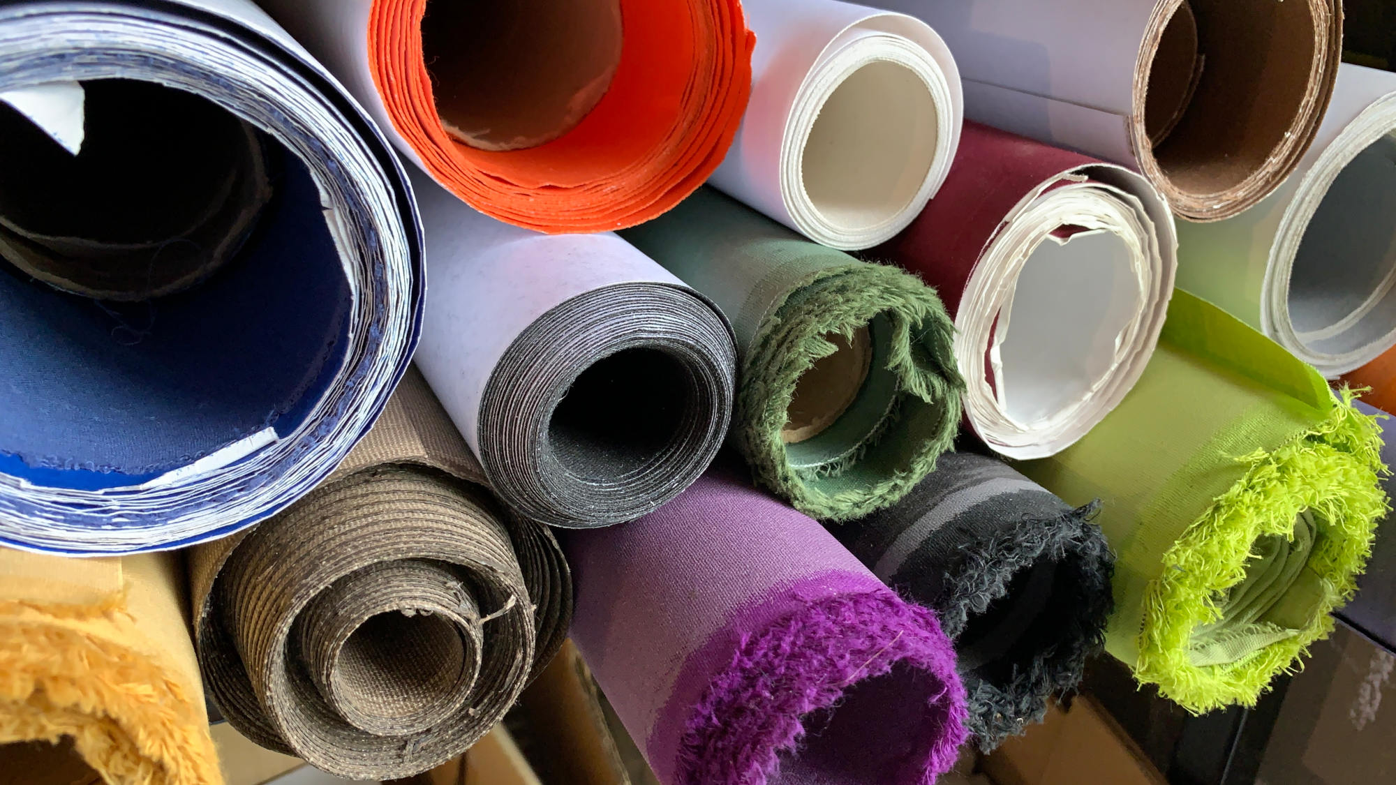Rolls of colored binding canvas, linen, stacked in a book bindery shelf.