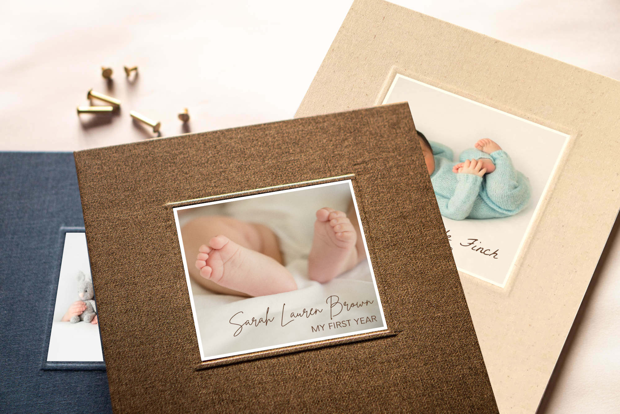 Personalized newborn memory books, set of 3, on a table top with brass screwposts and custom newborn photos on the covers.