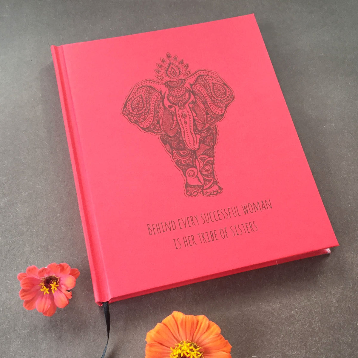 A red personalized journal cover with an elephant graphic on the front and the text "Behind every successful woman is a tribe of sisters" on a brown background with flowers.