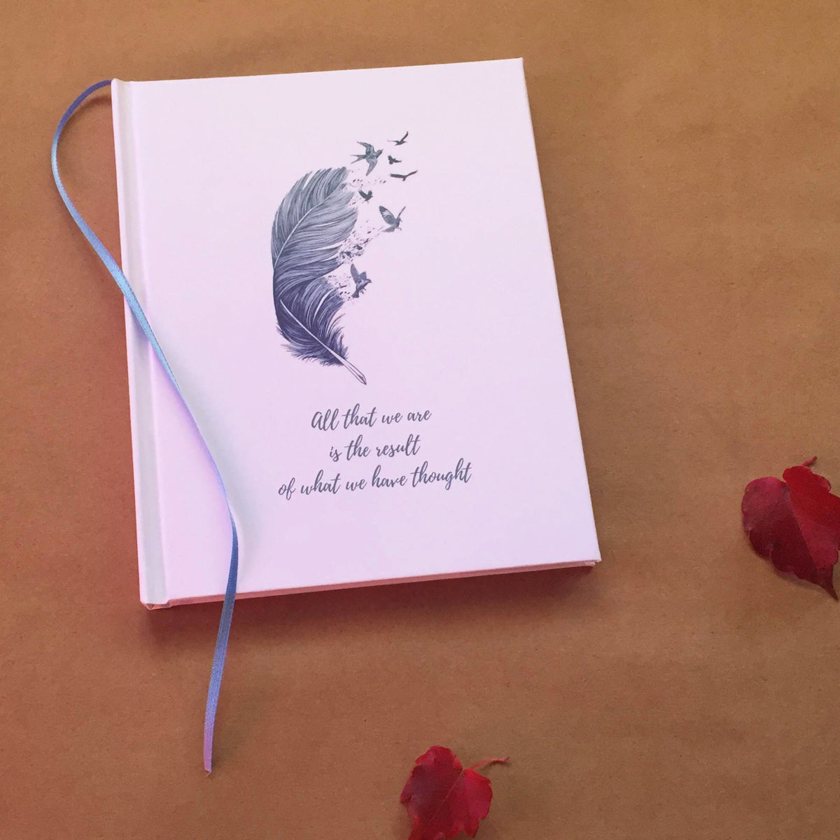 A white personalized cover with a feather and bird graphic and the quote "All that we are is the result of what we have thought" on a beige background with red leaves.