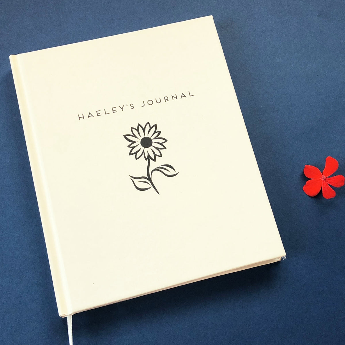 A personalized name journal with a white cover entitled "Haeley's Journal" with a flower graphic on a navy blue background.