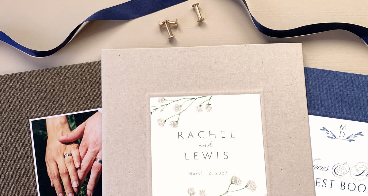 Three linen photo guest books for weddings on a beige table with personalized cover inlays. One is brown linen with an couple's photo of the bride and groom's hands and wedding rings. Another is cream linen and third is blue linen. These last two have personalized names and wedding date printed on inlay.'s