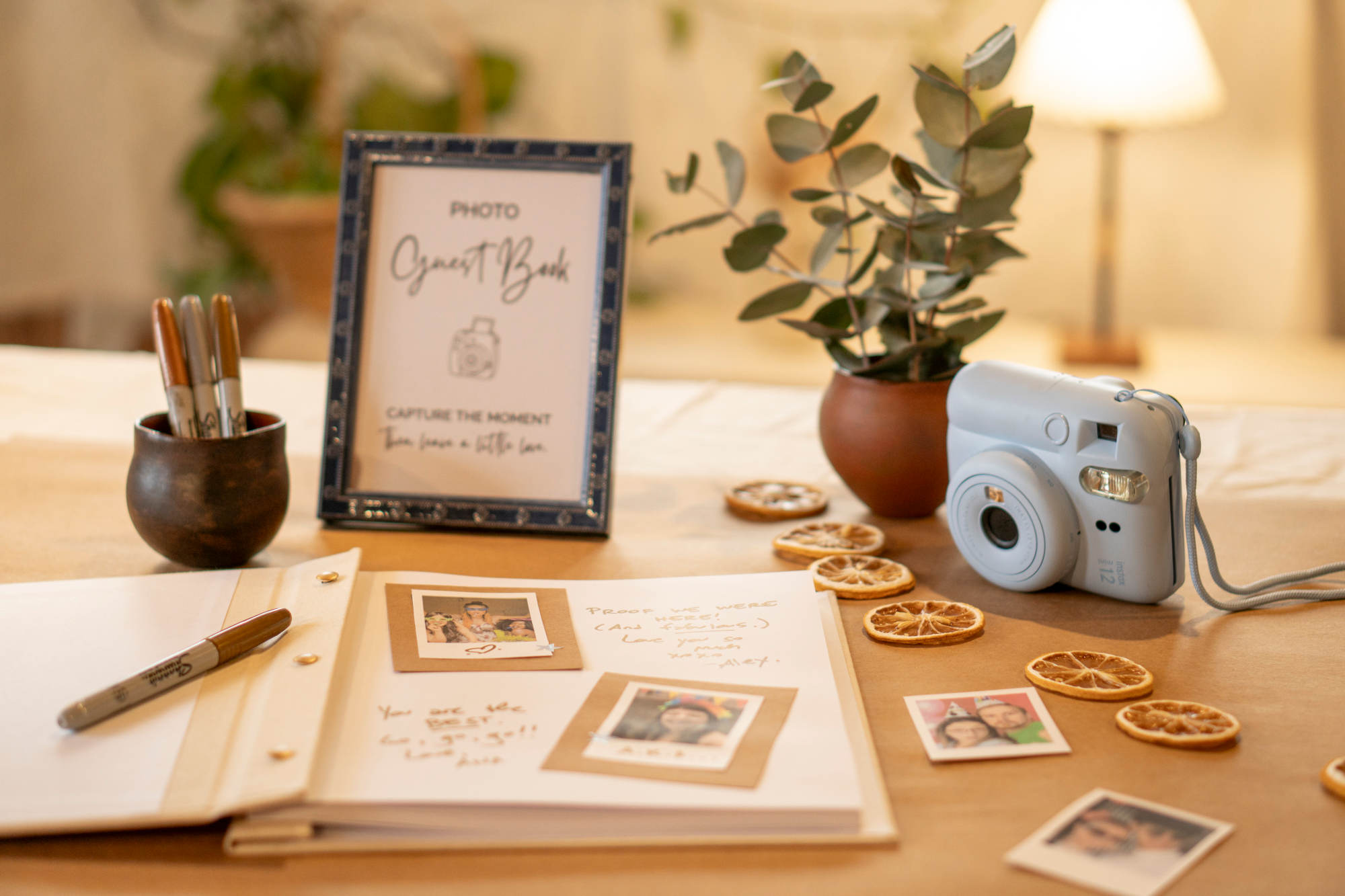 Gray instant camera on a party table with a photo guest book, framed table sign, and decorative items.