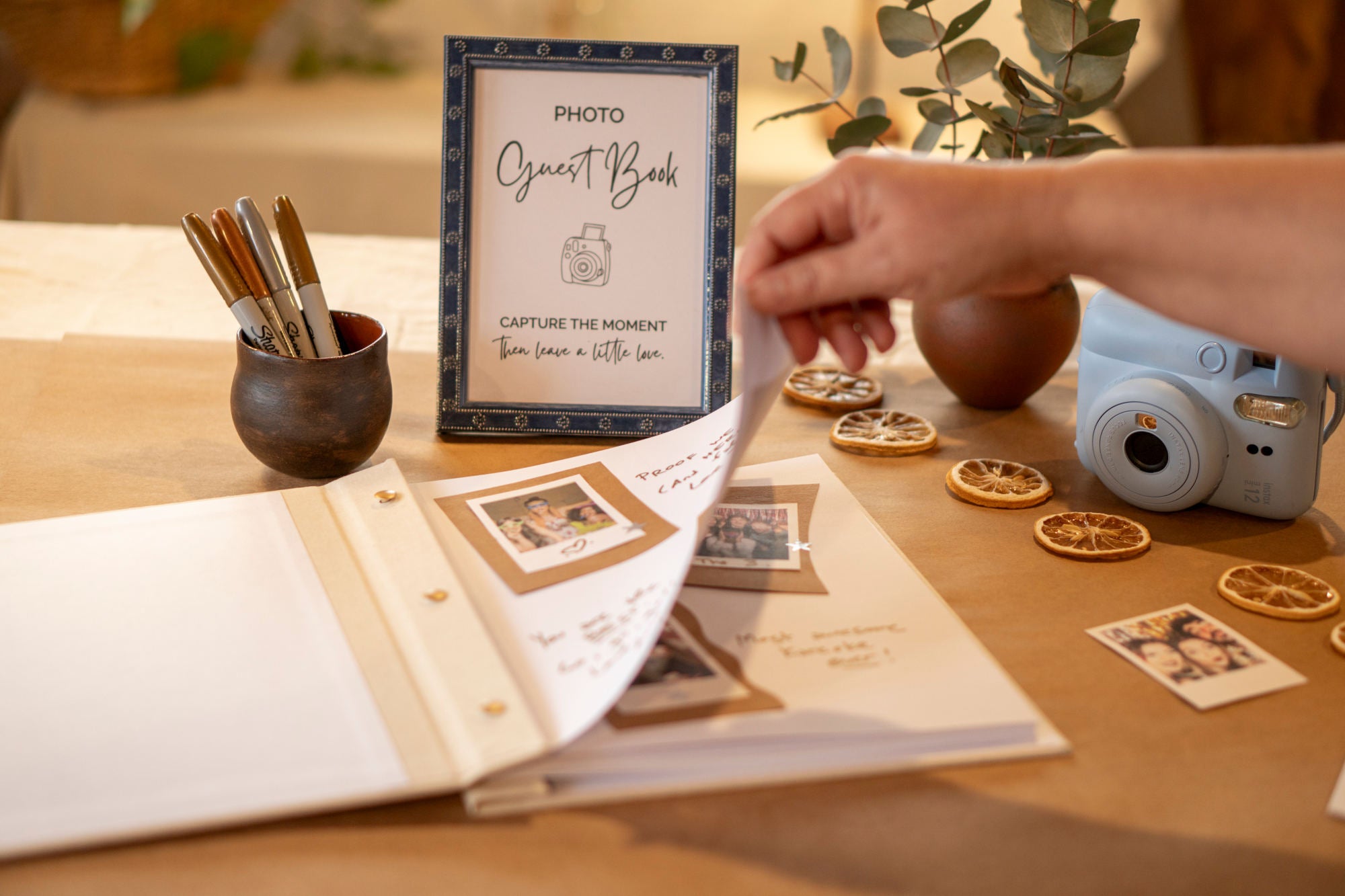 Person interacting with a photo gueset book on a decorated party table with a camera and stationery items.
