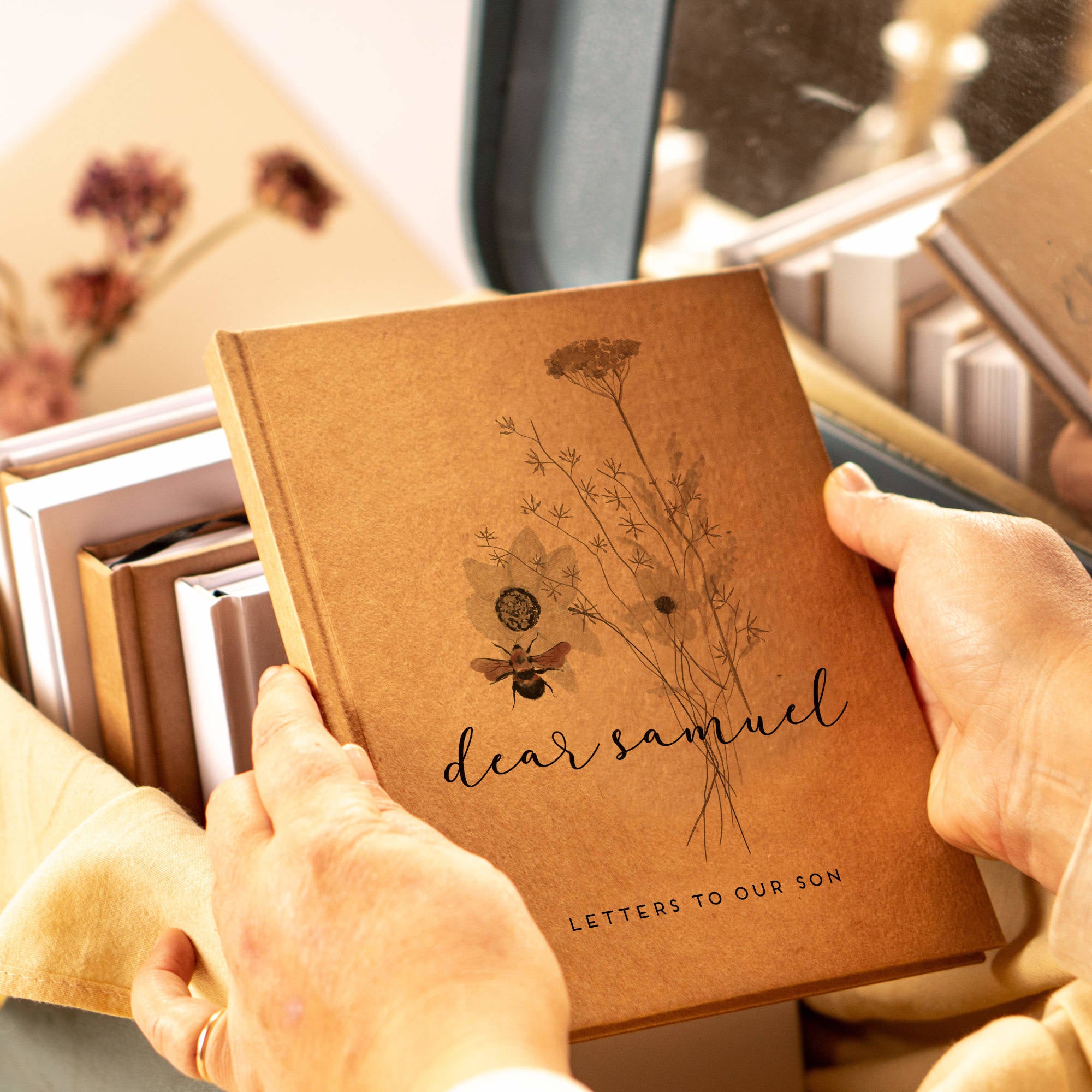 Hands holding a custom pregnancy planner journal in contemplation. The cover is personalized with the baby's name and a bouquet of wildflowers.