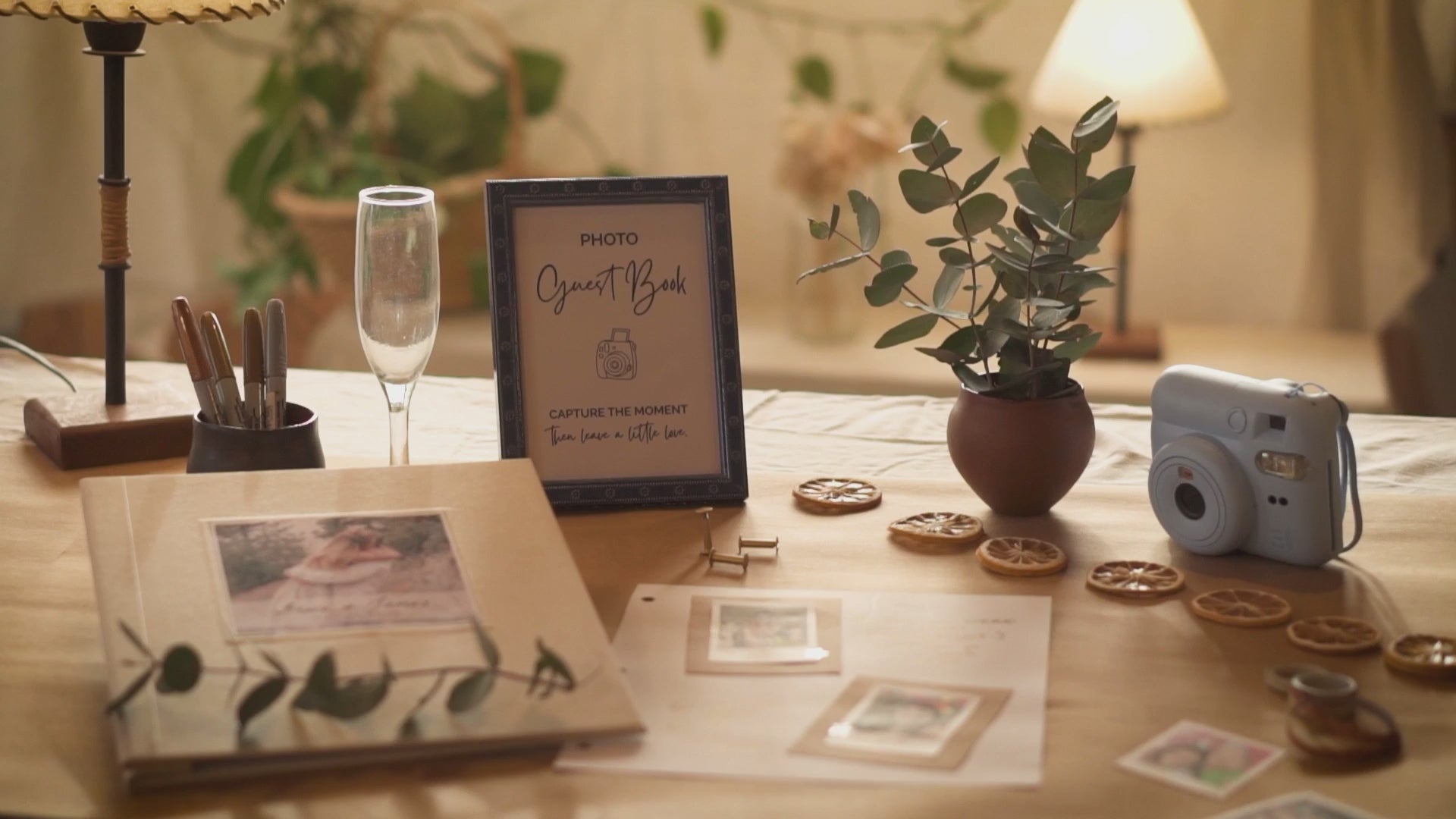 Load video: Short video of a photo guest book for wedding displayed and in use on a wedding guest book table with the removable pages being signed by guests on a table with a camera, pens, and wedding decorations.