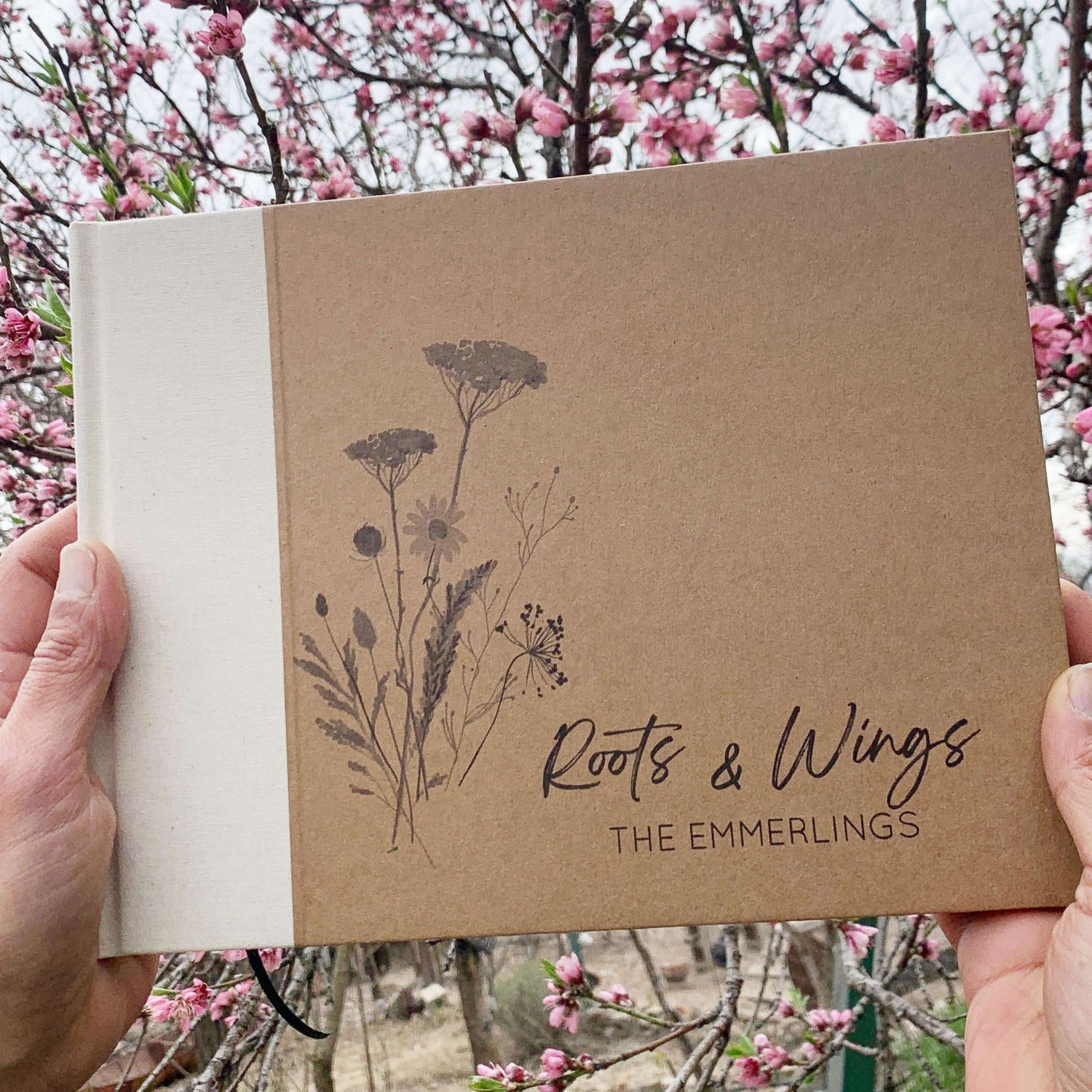 Person holding personalized retirement guest book with cream inen spine canvas. Hardback with personalized wildflower artwork cover design with custom names and text.