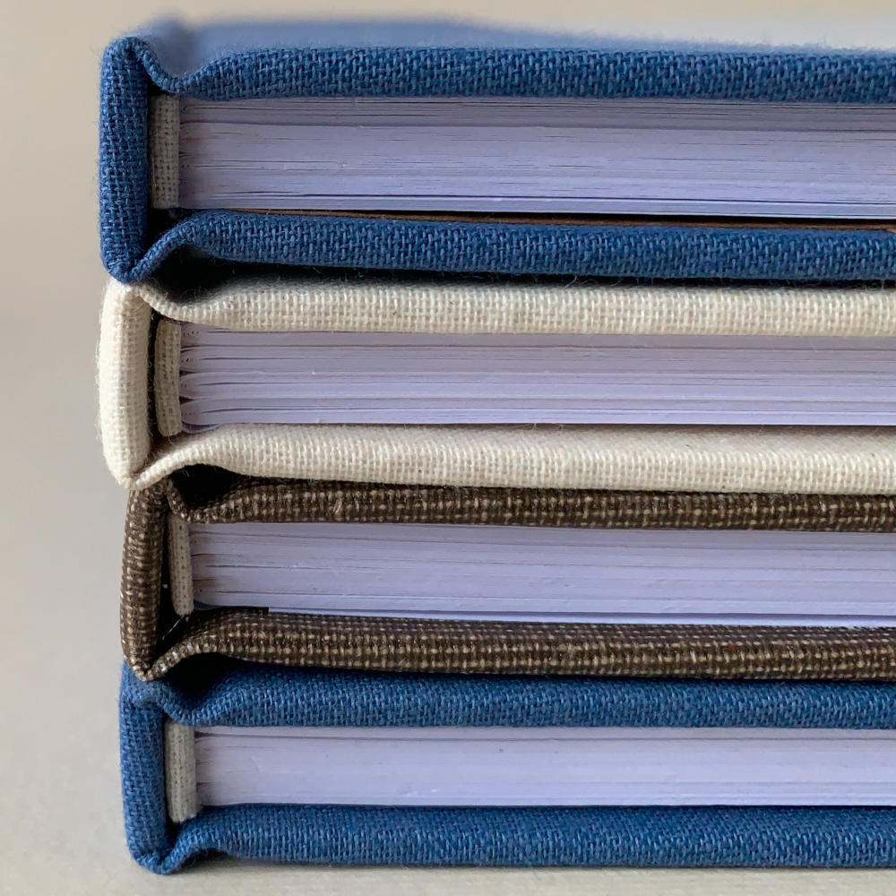 Stack of hand crafted hardback books showing headbands, folded folios and detail of linen binding canvas used.