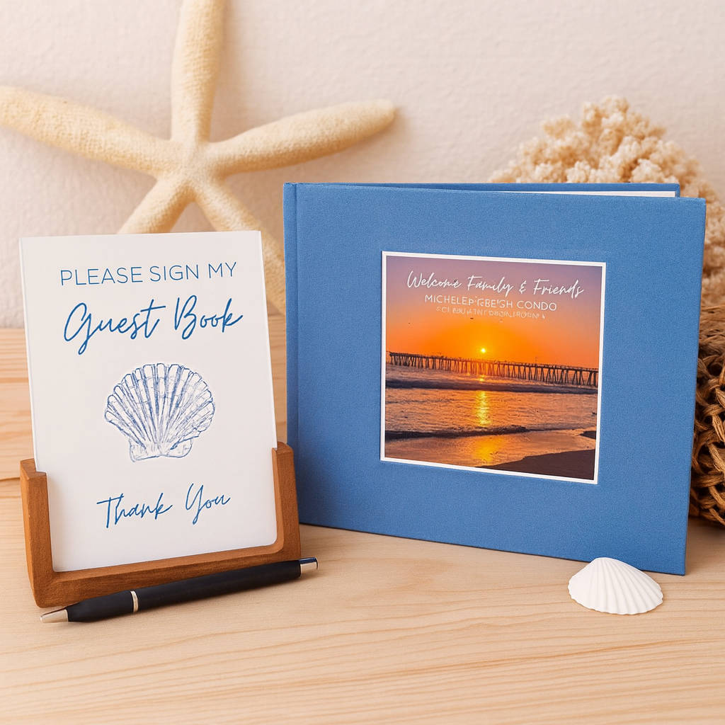 Blue custom beach house guest book with beach photo on cover, matching table sign to encourage guest involvement, and pen on wooden surface with starfish and shell decor.
