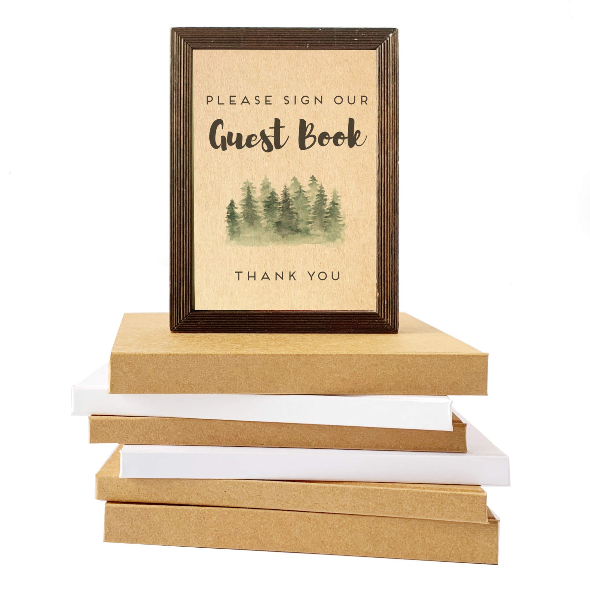 Stack of kraft paper books with a framed sign on top, featuring a forest design and text. The frame holds a custom table sign for guest books, encouraging guests to sign the welcome book.
