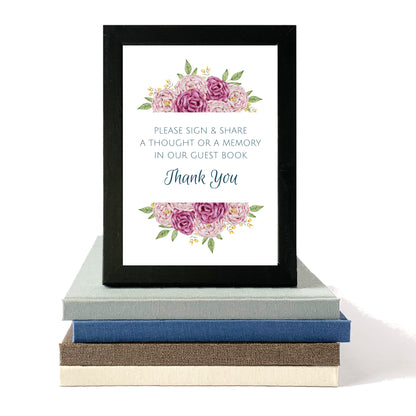 Framed guest book sign with floral design and text on a stack of books.
