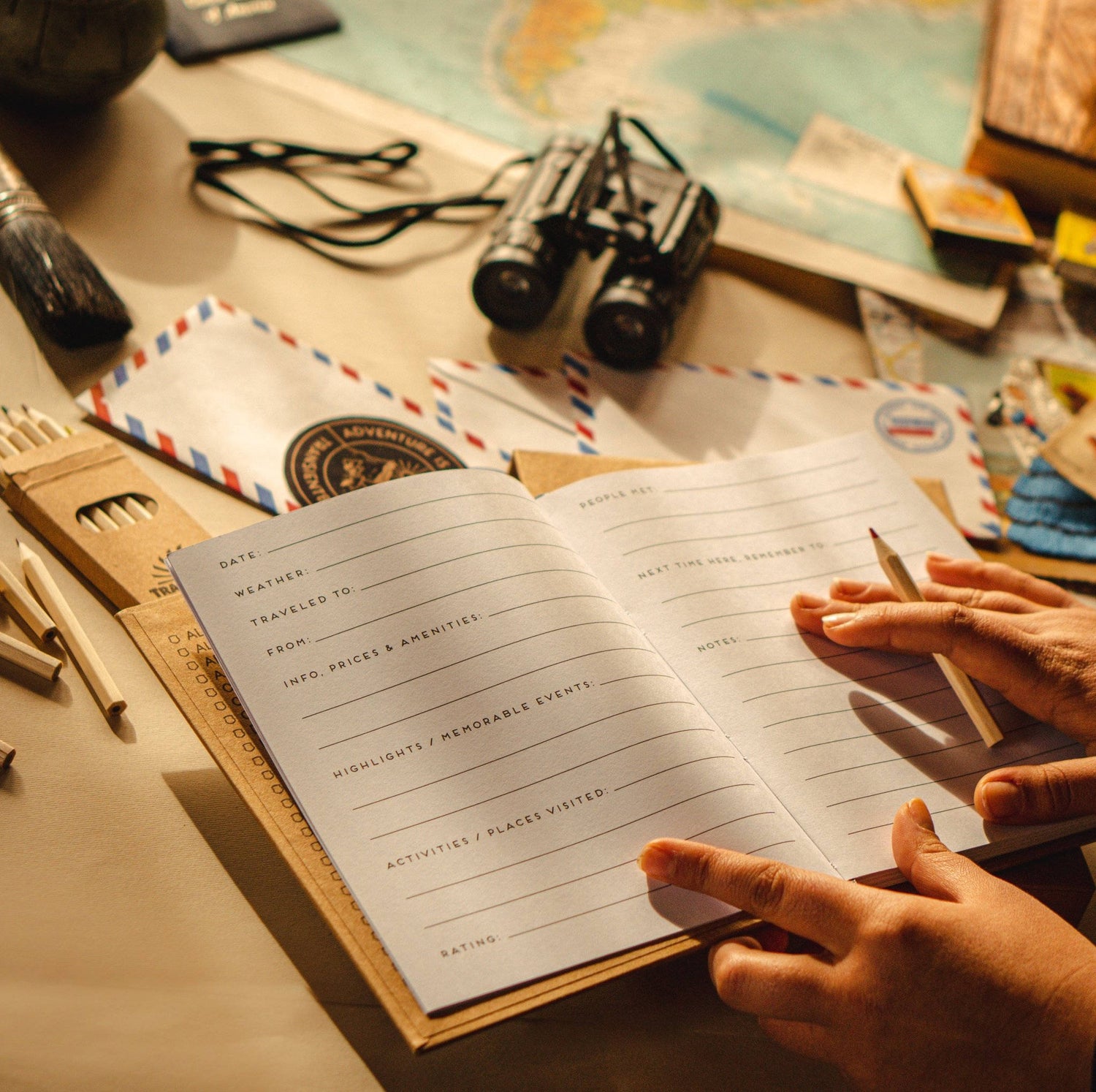 Travel journal with prompts open on a table being used by a traveler on a table full of travel gear and accessories. 