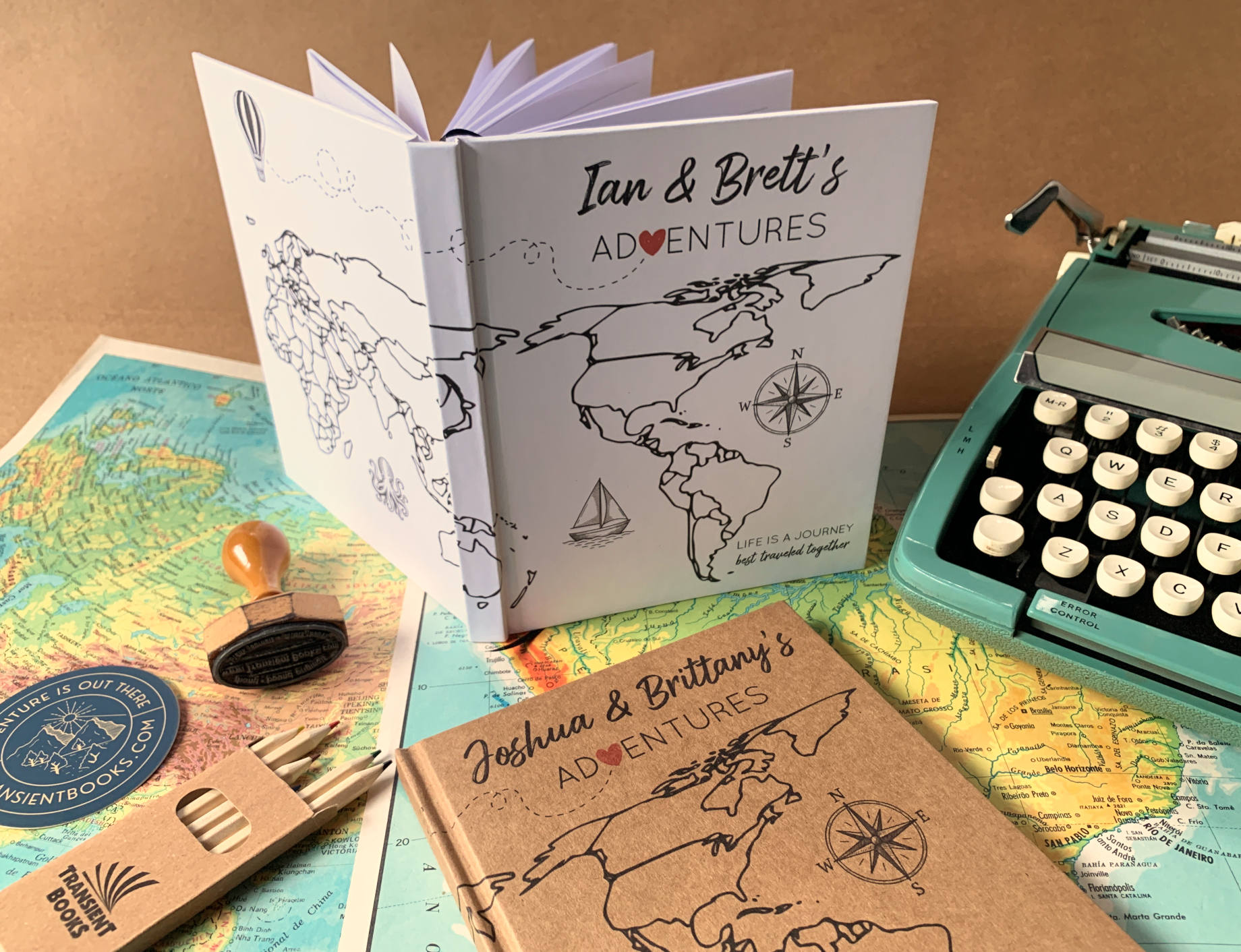 Personalized world travel journals for couples, hand crafted, staged on a table with typewriter, colored pencils and maps.