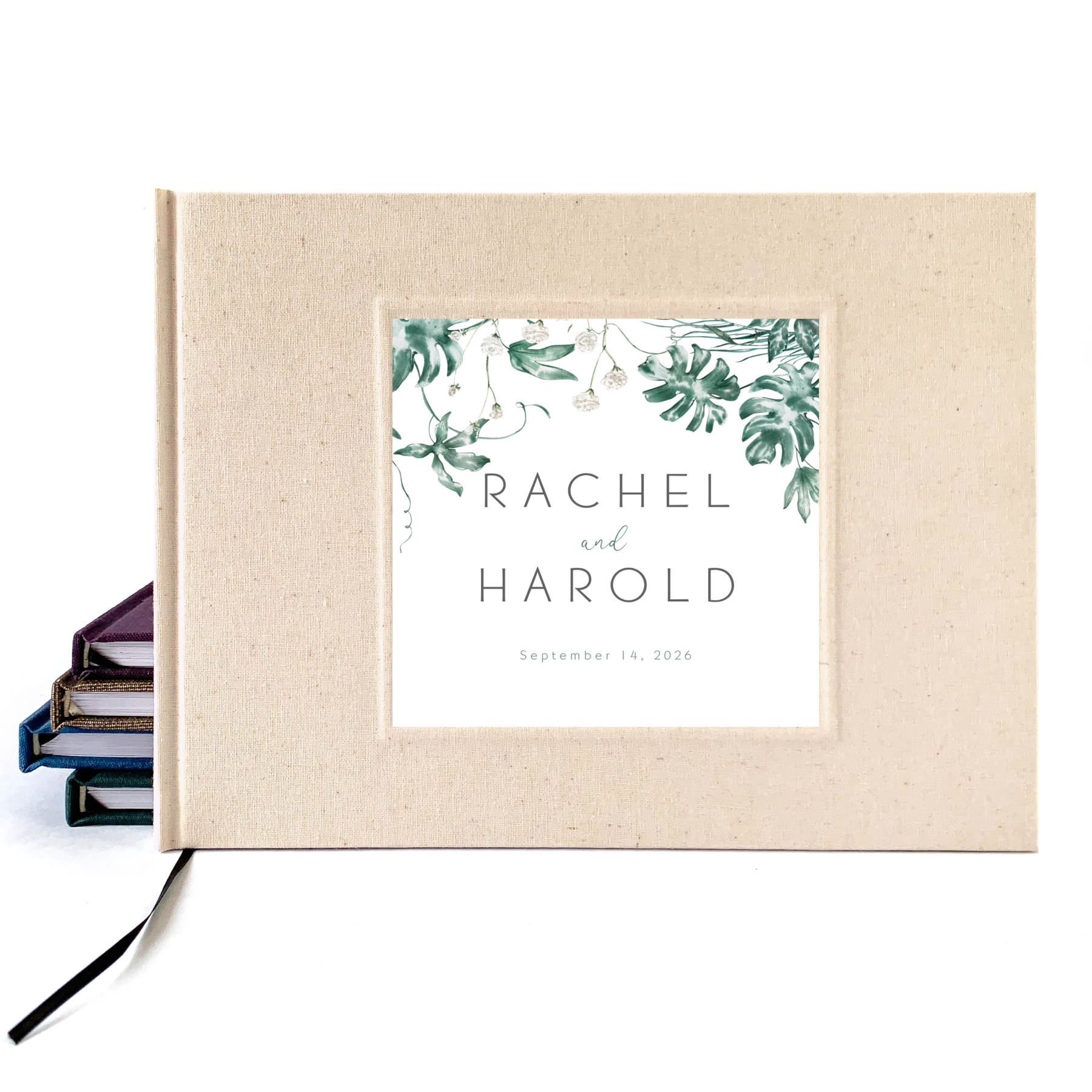 Tropical wedding guest book with printed inlay leaf design and custom names on a cream linen cover.