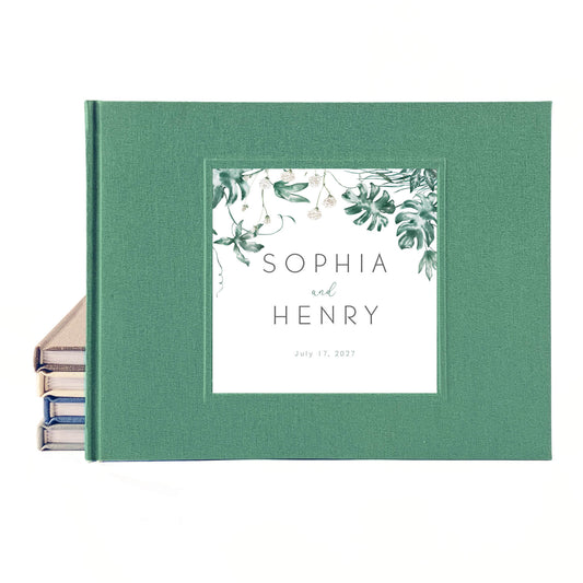 Tropical wedding guest book with printed inlay leaf design and custom names on a green linen cover.