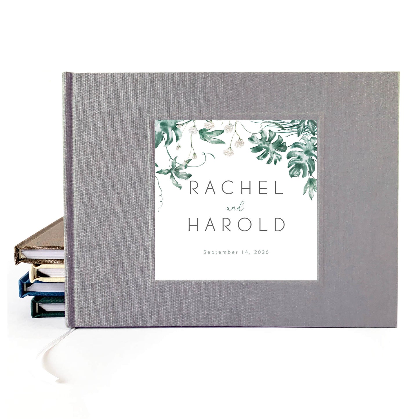 Tropical wedding guest book with printed inlay leaf design and custom names on a gray linen cover.