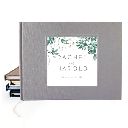 Tropical wedding guest book with printed inlay leaf design and custom names on a gray linen cover.