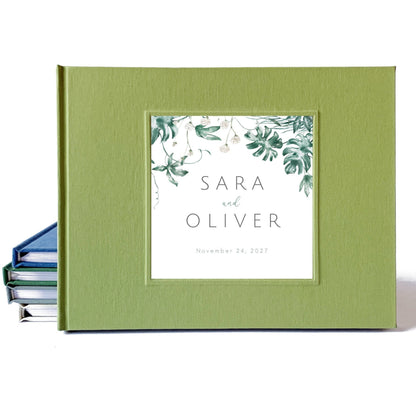 Personalized tropical wedding guest book with a green linen cover, and the bride and groom's names surrounded by tropical leaves.