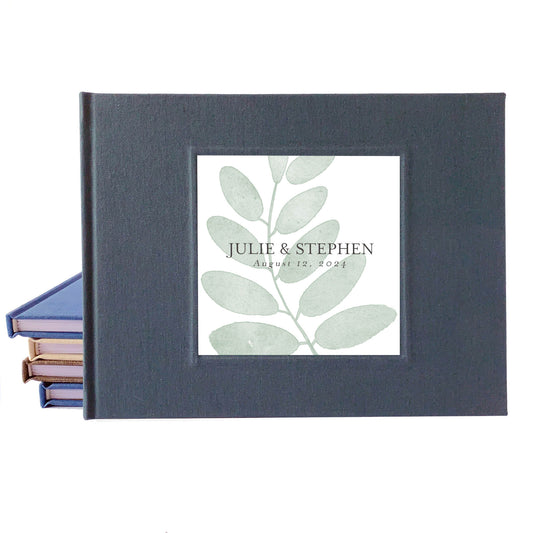 Rustic wedding guest book with printed inlay leaf design and custom names on a dark gray linen cover.