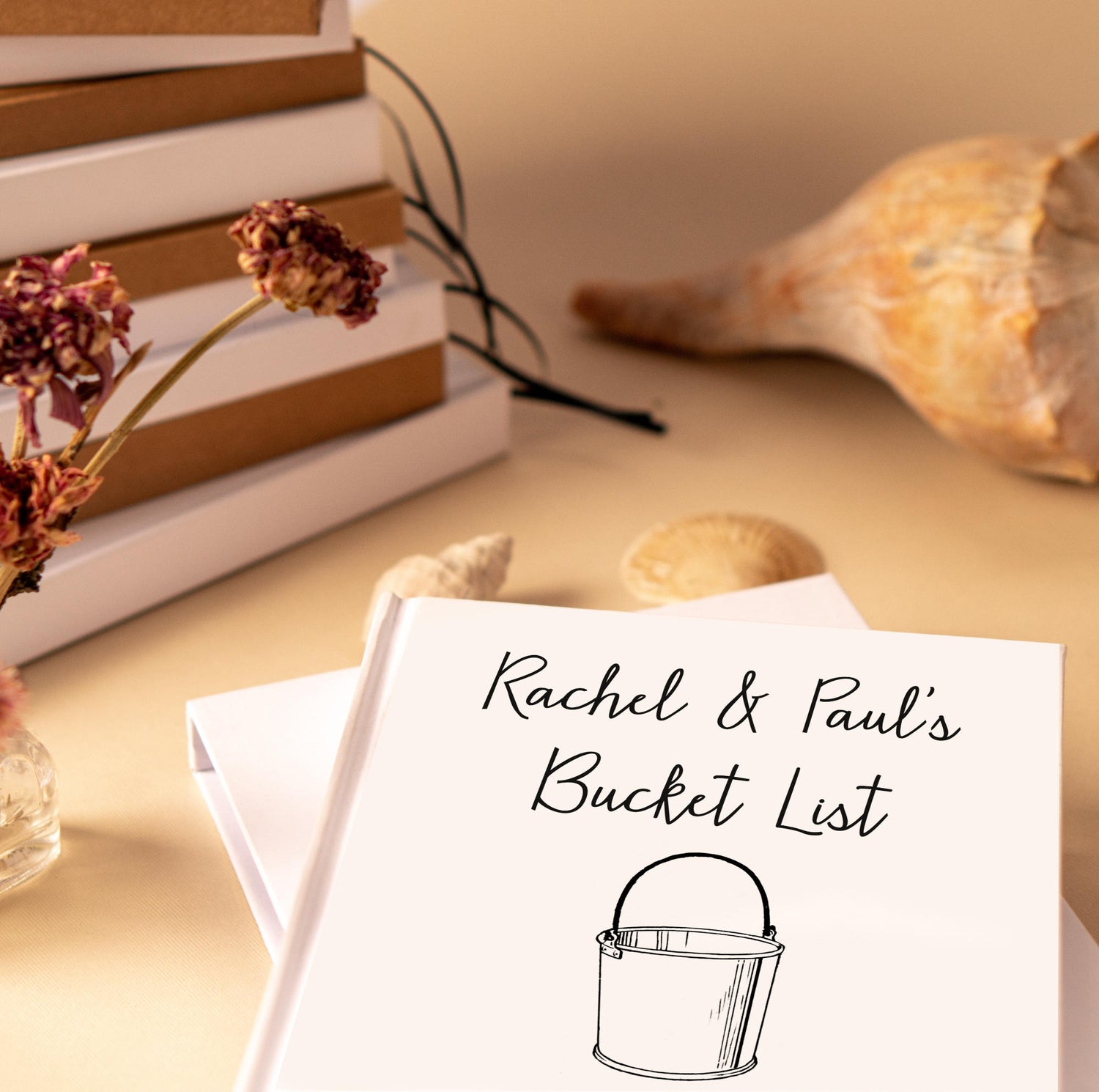 A white bucket list book laying on a table, ready to be used. The cover of the handbound book is white, personalized with their names. 